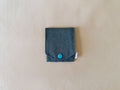 A small dark teal fabric pouch with a flap closure and a bright turquoise snap button, shown on a light beige textured background.